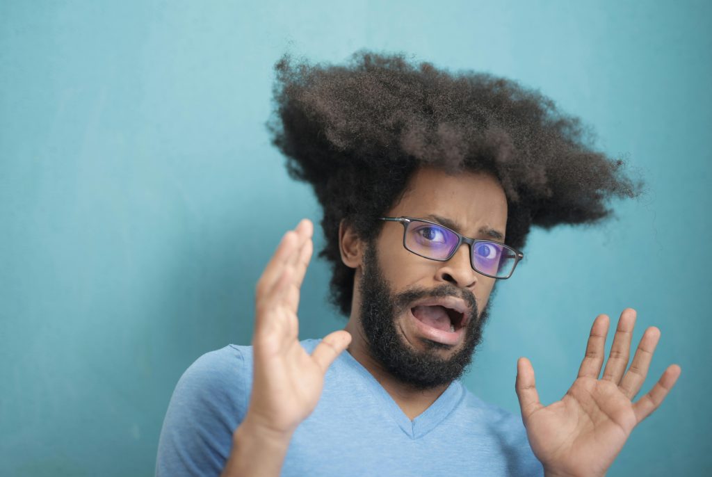 Portrait of a surprised man with afro hair and glasses, expressing shock with a blue background.